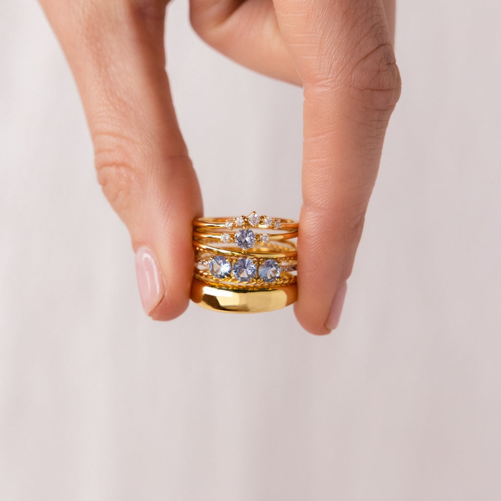 A hand displays the Aquamarine Stacking Ring Set, featuring boho rings with ocean blue gemstones, against a neutral background.
