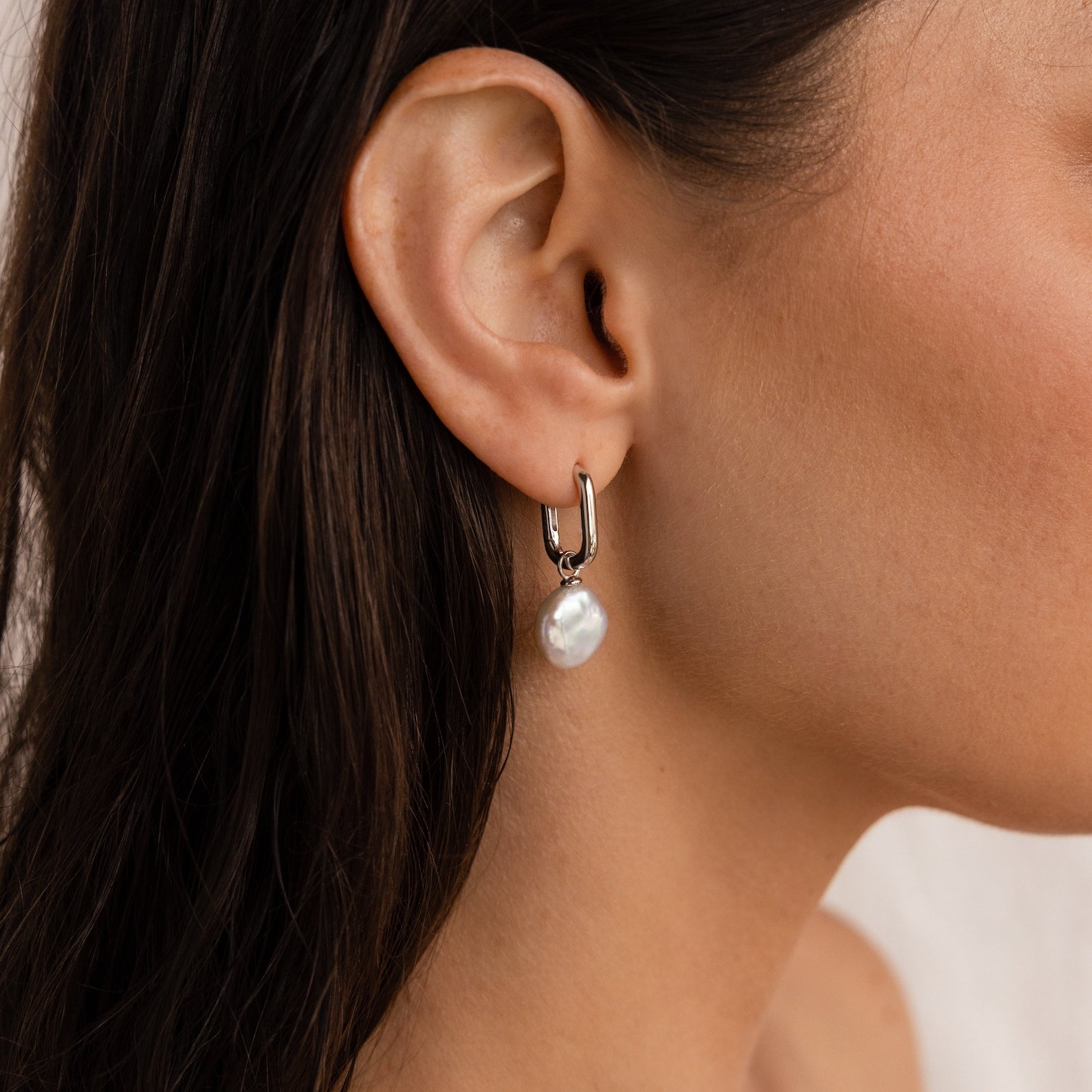 Close-up of a woman's ear wearing the Bridget Pearl Hoops—silver huggie earrings featuring elegant white pearl charms.