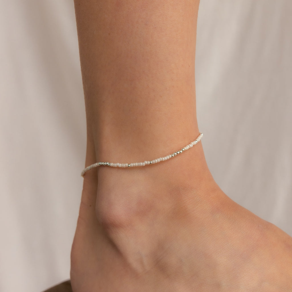 The Dainty Pearl Beaded Anklet, adorned with delicate pearls, graces the ankle and is elegantly displayed against a soft, neutral background.