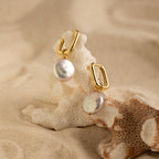 Bridget Pearl Hoops showcase elegant pearl charms on delicate huggie hoops, artfully displayed atop coral and surrounded by sand.
