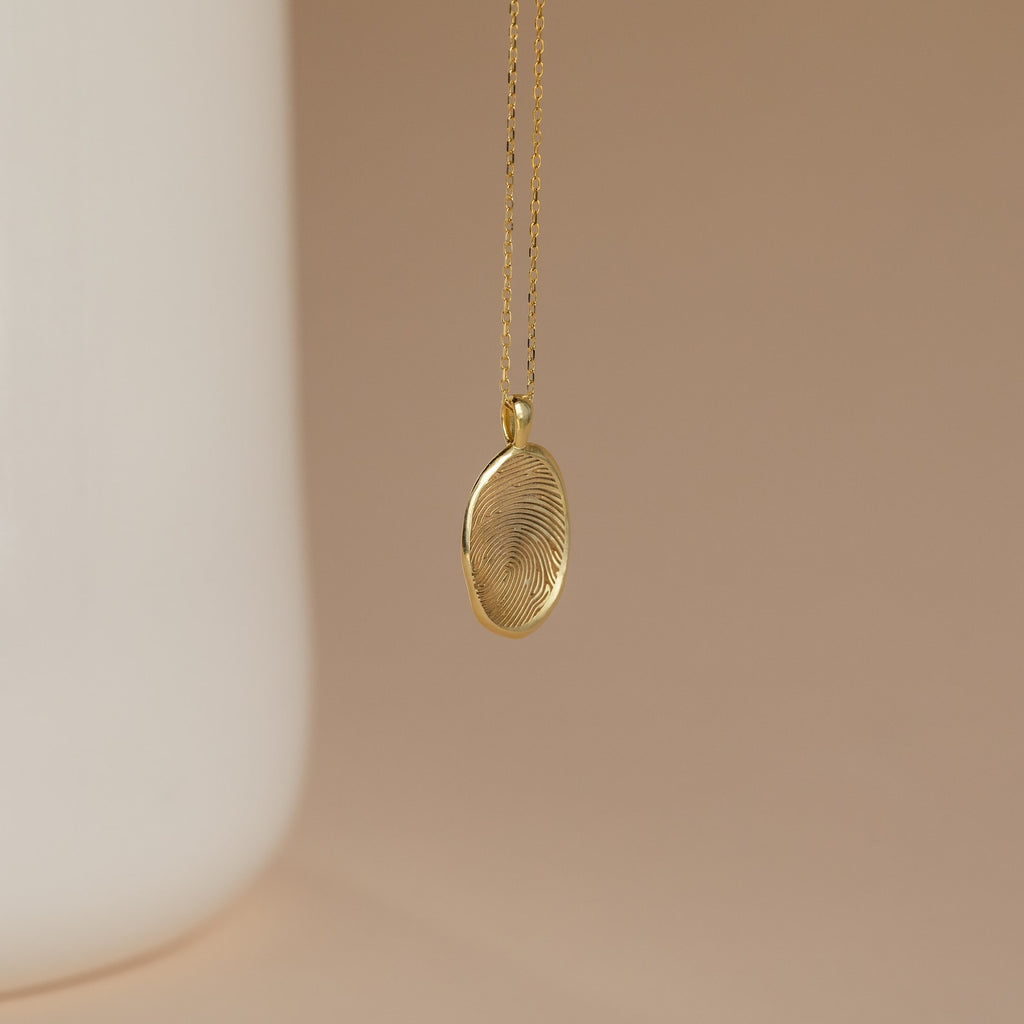 The Custom Fingerprint Necklace in Rose Gold features an engraved pendant with your unique fingerprint—a sentimental gift, beautifully displayed against a soft beige background.