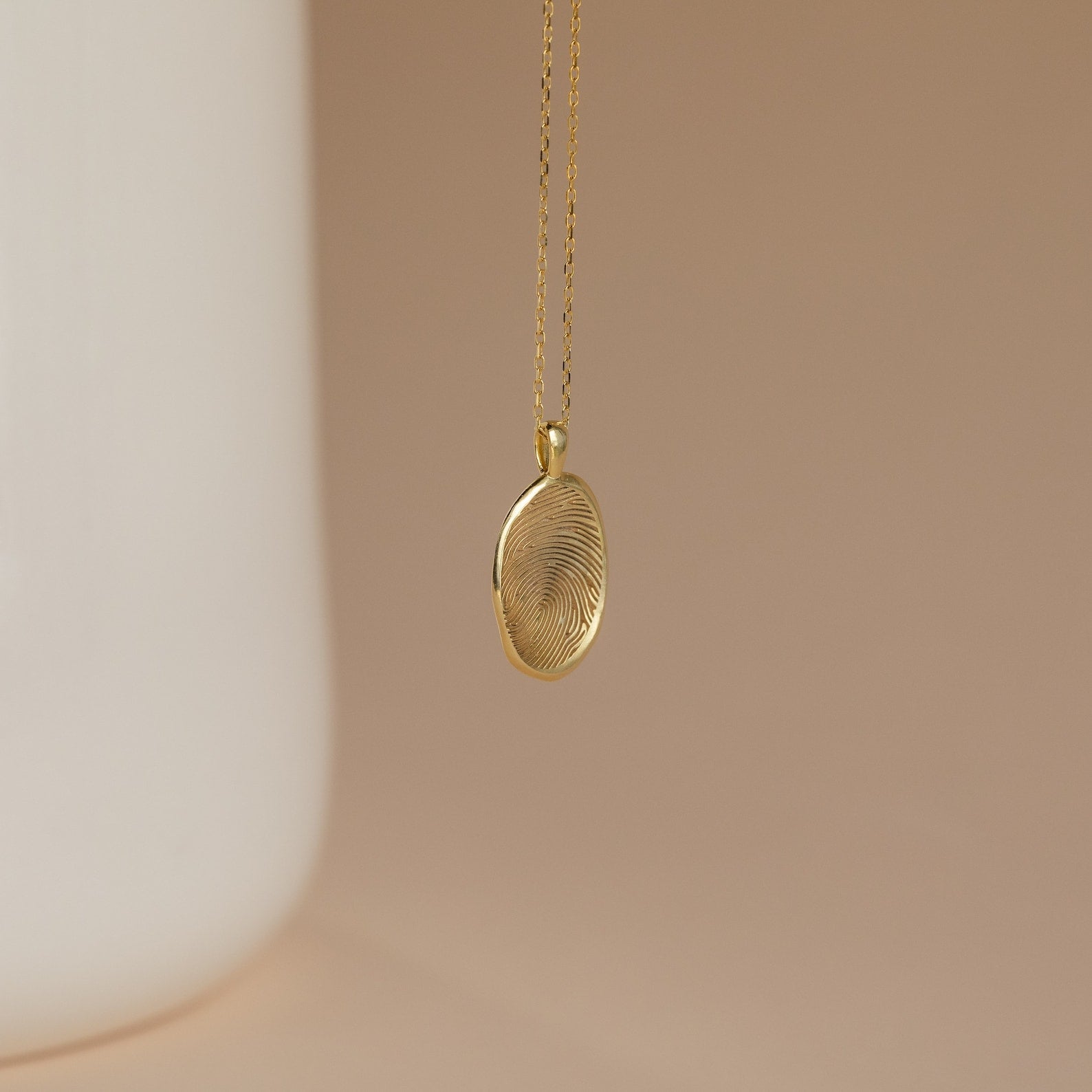 The Custom Fingerprint Necklace in Rose Gold features an engraved pendant with your unique fingerprint—a sentimental gift, beautifully displayed against a soft beige background.