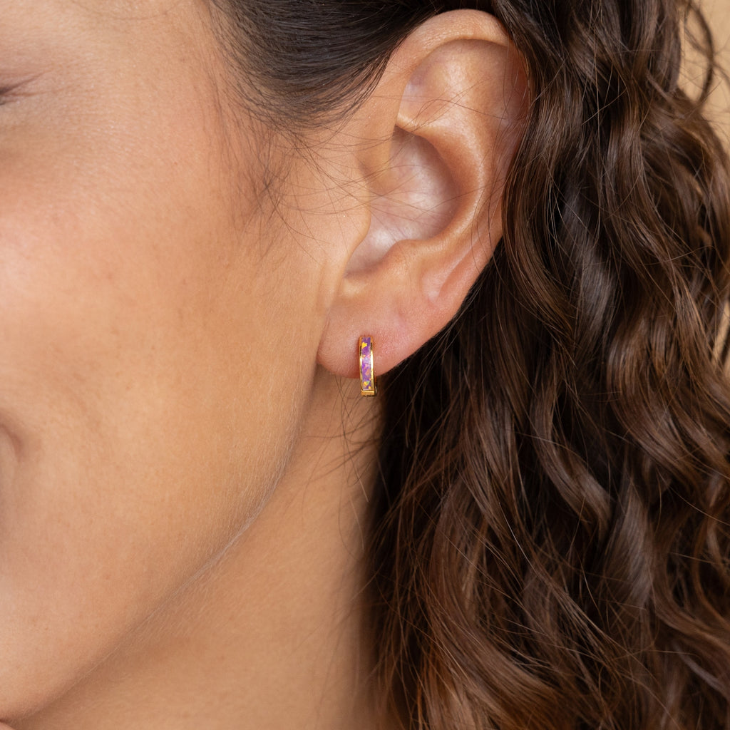 Close-up of a woman's ear with curly hair, wearing Pastel Opal Inlay Huggies—small earrings featuring colorful opal inlay.