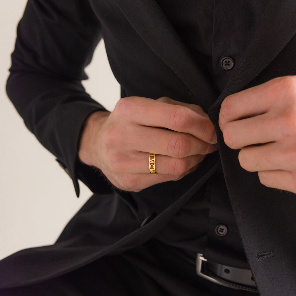 A person in a black suit buttons their jacket, wearing the Roman Numerals Ring in 18K Gold with engraved details, highlighting a personalized milestone or meaningful date.