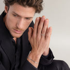 Man in a black suit, hands together, wearing silver rings—including the Roman Numerals Ring in Sterling Silver—and a bracelet, looking thoughtfully downward.