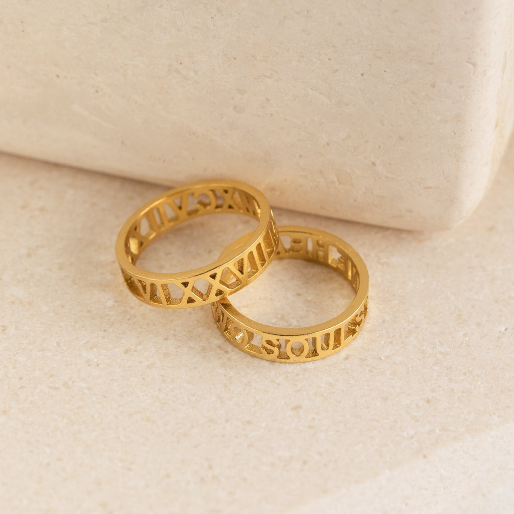 Two Roman Numerals Rings rest on a smooth, light surface, perfect as personalized milestone jewelry.