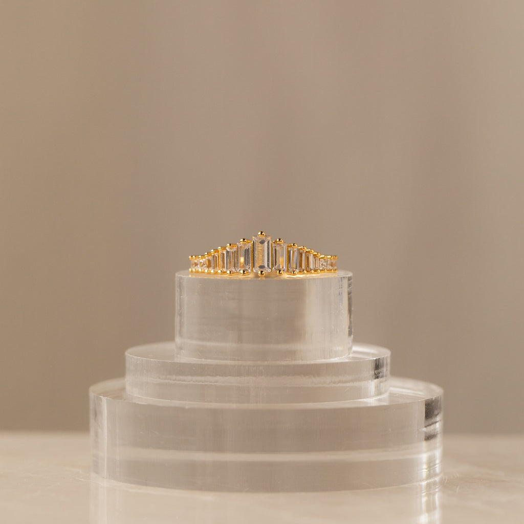 The Art Deco Diamond Ring, featuring rectangular diamonds and a striking chandelier silhouette, is displayed on a clear acrylic stand against a neutral background as a true statement piece.