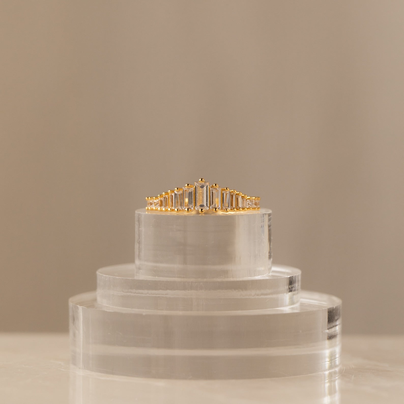 The Art Deco Diamond Ring, featuring rectangular diamonds and a striking chandelier silhouette, is displayed on a clear acrylic stand against a neutral background as a true statement piece.