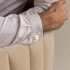 A man’s arm rests on a chair, his white shirt accessorized with Engraved Cufflinks—gold, personalized, and etched with “MMK.”.