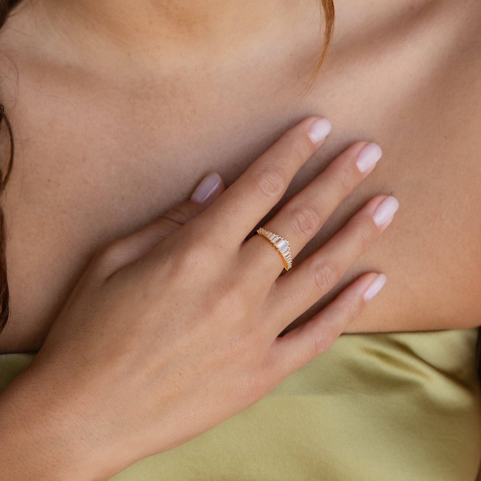 A woman's hand wearing the Art Deco Diamond Ring rests on her chest in a light yellow top—the ring shines beautifully as a standout accessory.