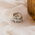 Two Thick Handwriting Bands with engraved messages rest on soft white fabric beside a ribbed amber glass—ideal minimalist jewelry for any style.
