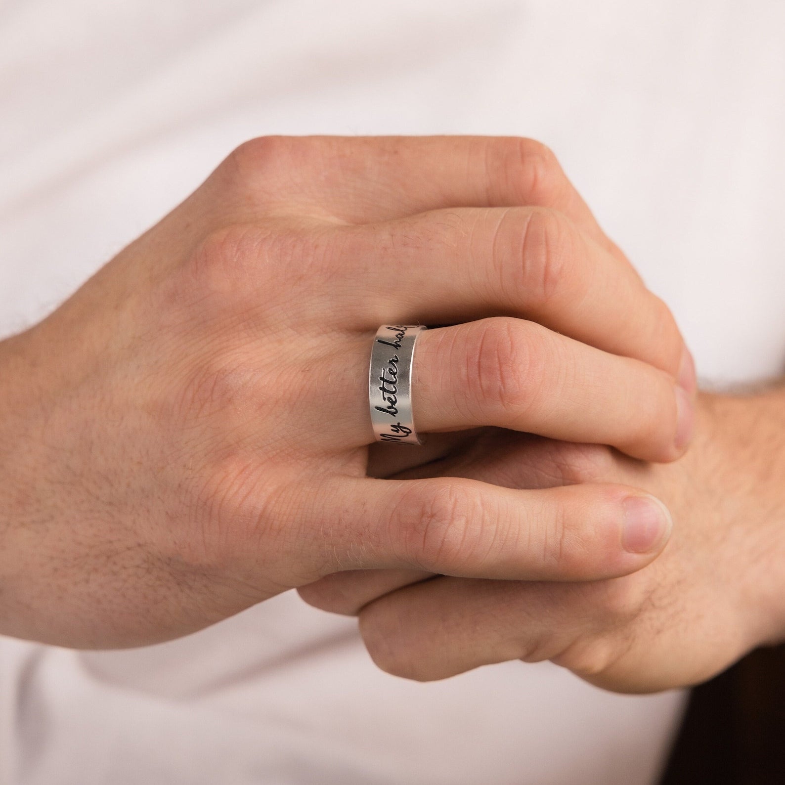 A person wearing a silver Thick Handwriting Band with engraved text, hands gently clasped together—an elegant piece of minimalist jewelry.