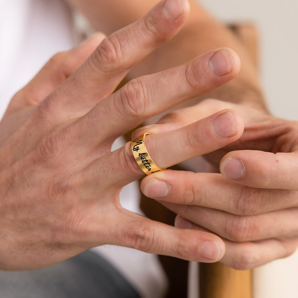 A person slides a gold Thick Handwriting Band with script engraving onto their finger, embracing the elegance of minimalist jewelry.