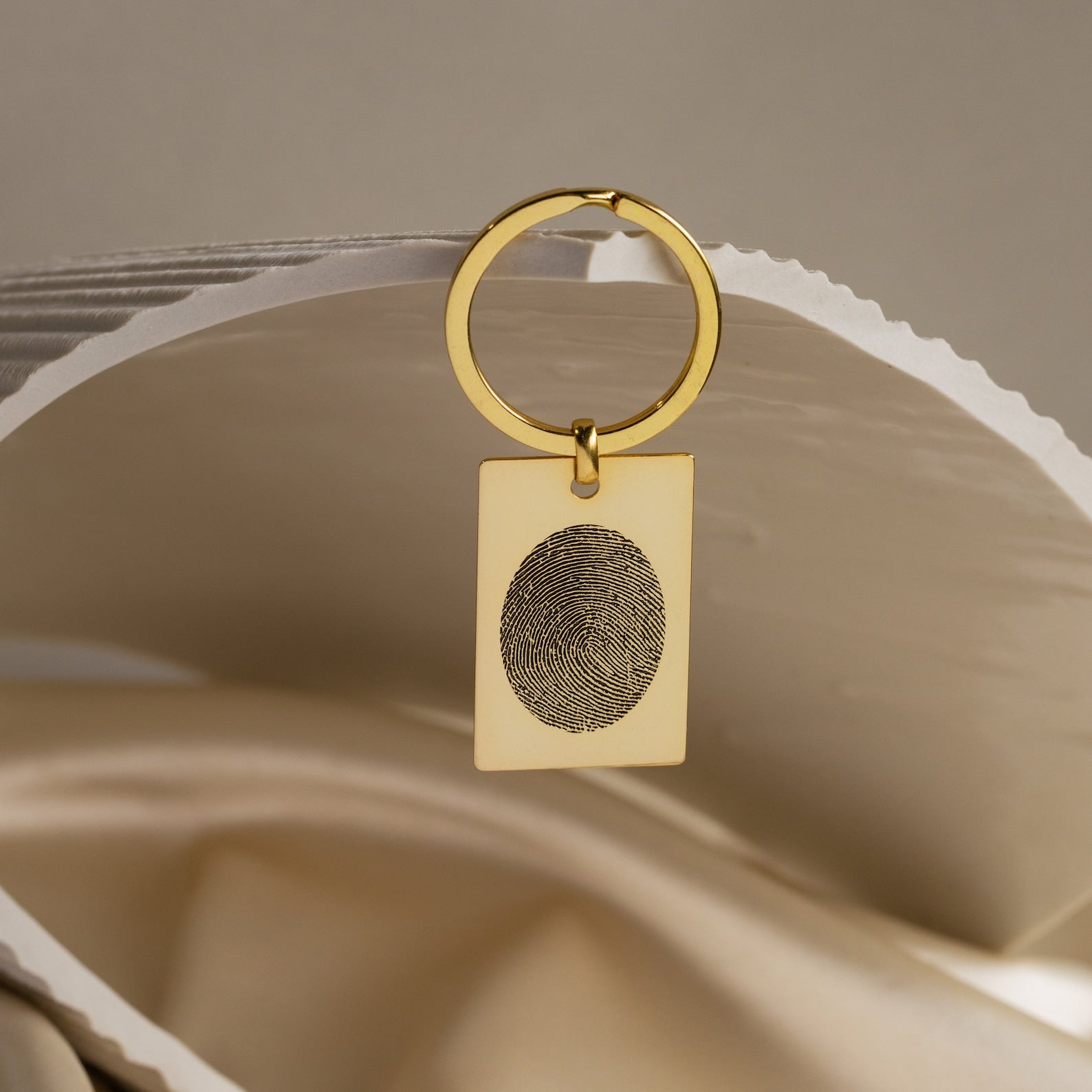 The Fingerprint Rectangle Keychain features a gold rectangular pendant engraved with your unique fingerprint, displayed on a folded white surface—a personalized keepsake perfect for cherishing special memories.