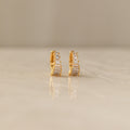 Close-up of a pair of gold Art Deco Huggie earrings on a marble surface, featuring a symmetrical arrangement of baguette and round-cut diamonds for a tiered, structured look.
