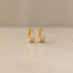 Close-up of a pair of gold Art Deco Huggie earrings on a marble surface, featuring a symmetrical arrangement of baguette and round-cut diamonds for a tiered, structured look.