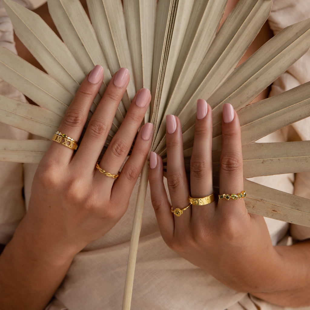 Hands wearing gold 3D Name Band rings with intricate designs on a neutral background.