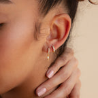 Close-up of a woman's ear wearing Raine Opal Dagger Huggies, her hand gently touching her neck against a neutral background.