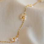 The Flower Pearl Station Necklace, featuring delicate pearl flower charms on a gold chain, is displayed on soft white fabric—a beautiful bridesmaids gift for your special day.