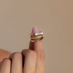 A hand displays three Thin Name Signet Rings—engraved with Nova, Charlotte, and Aidan—stacked on the index finger against a beige background.