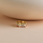 The Thin Name Signet Ring features a modern bar design and can be stacked in gold, silver, and rose gold, each engraved with names like Oliver, Nova, or Isabelle for a personalized touch.