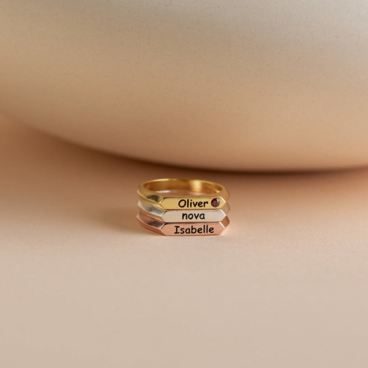 The Thin Name Signet Ring features a modern bar design and can be stacked in gold, silver, and rose gold, each engraved with names like Oliver, Nova, or Isabelle for a personalized touch.