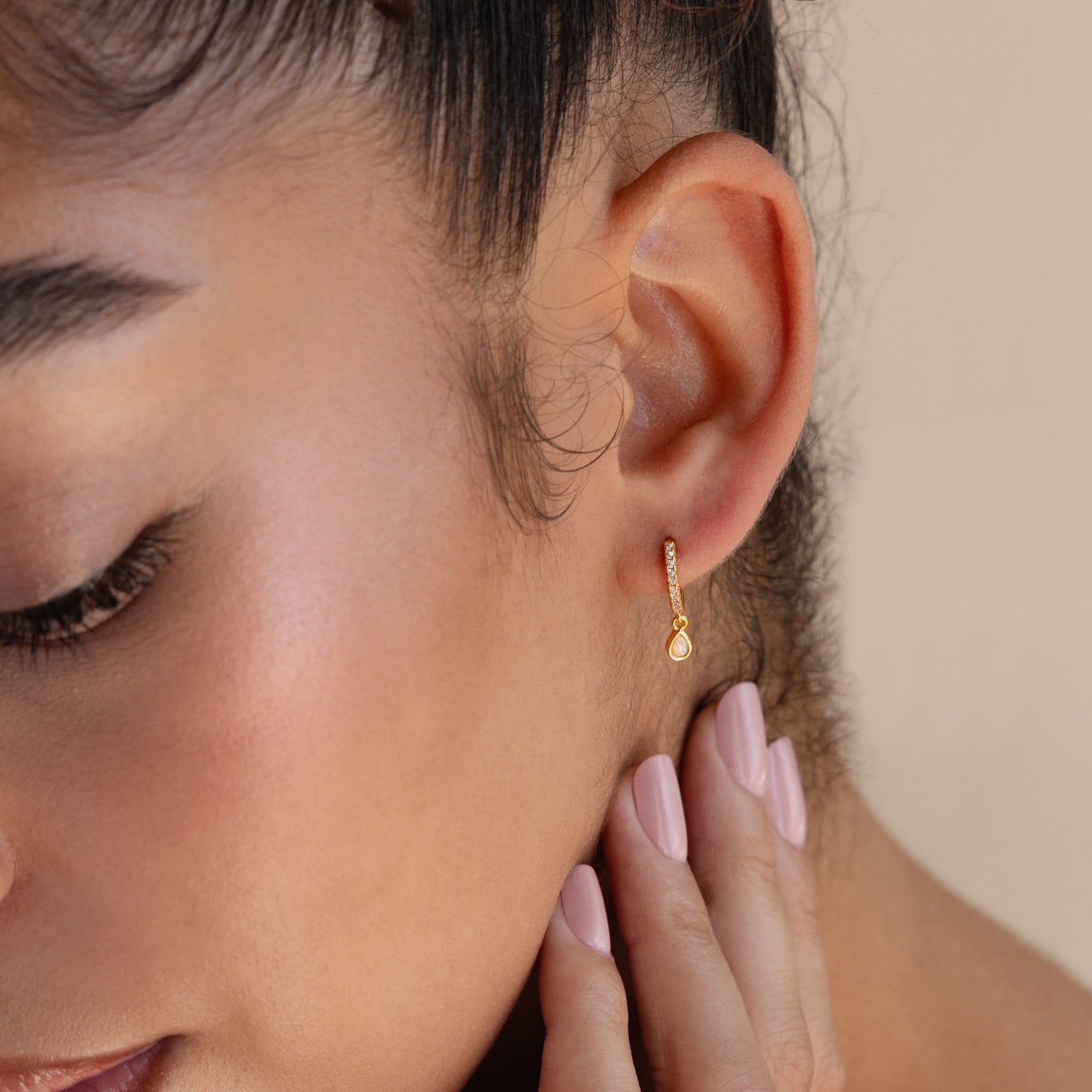 A close-up of a woman's ear adorned with elegant Opal Drop Huggies.