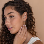 Woman with curly hair wears Ocean Opal Inlay Huggies, touching her neck and gazing to the side—a stylish choice for weddings or everyday elegance.