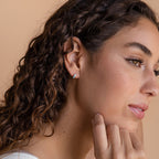 A woman with curly hair and a hand on her chin models the elegant Ocean Opal Inlay Huggies.