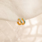 Two Ocean Opal Inlay Huggies rest on soft fabric—perfect as delicate wedding jewelry or a subtle accent alongside favorites like the Light Blue Opal Huggie Hoops.