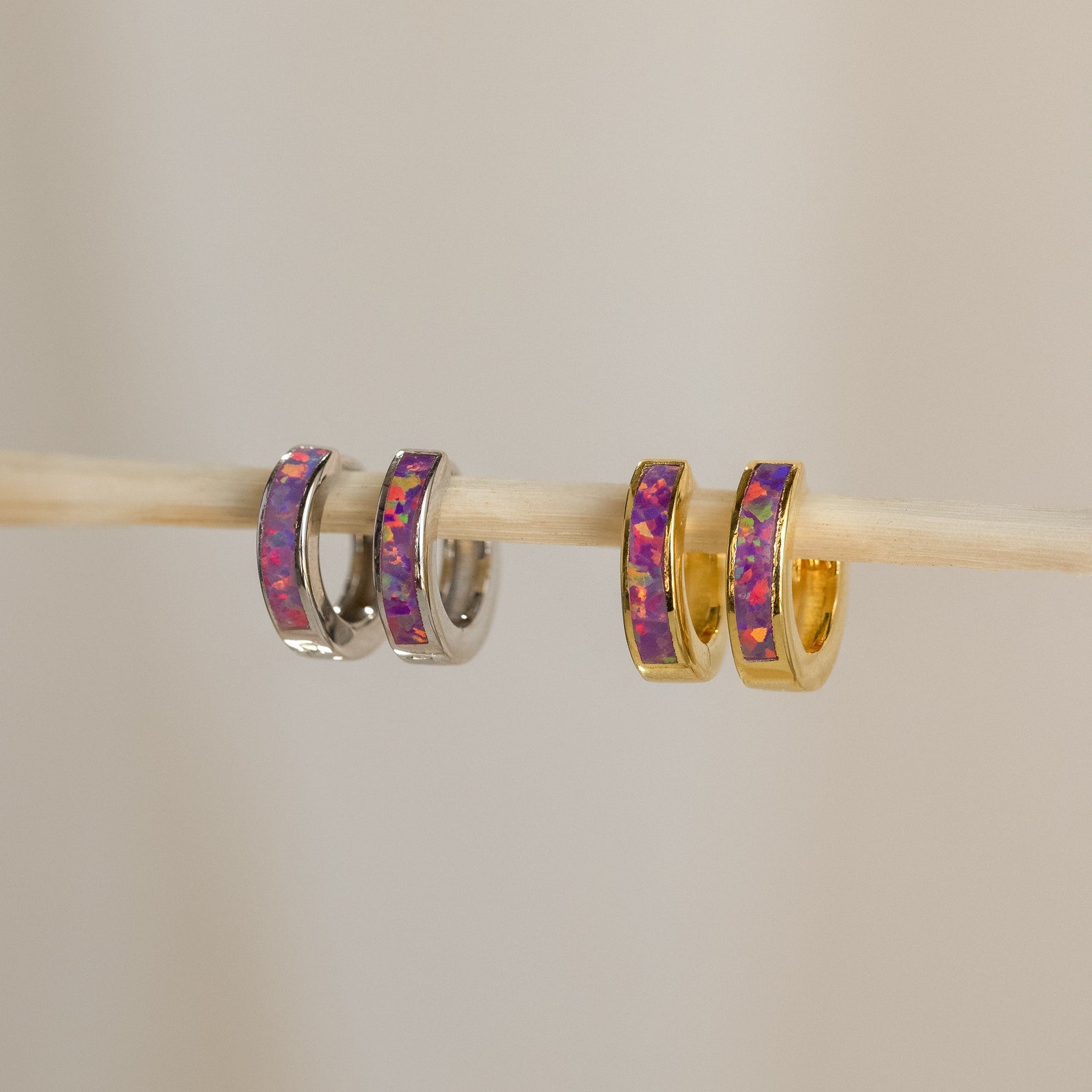 Lavender Opal Inlay Huggies, minimalist hoop earrings with a subtle purple opal shimmer, are displayed together on a stick.