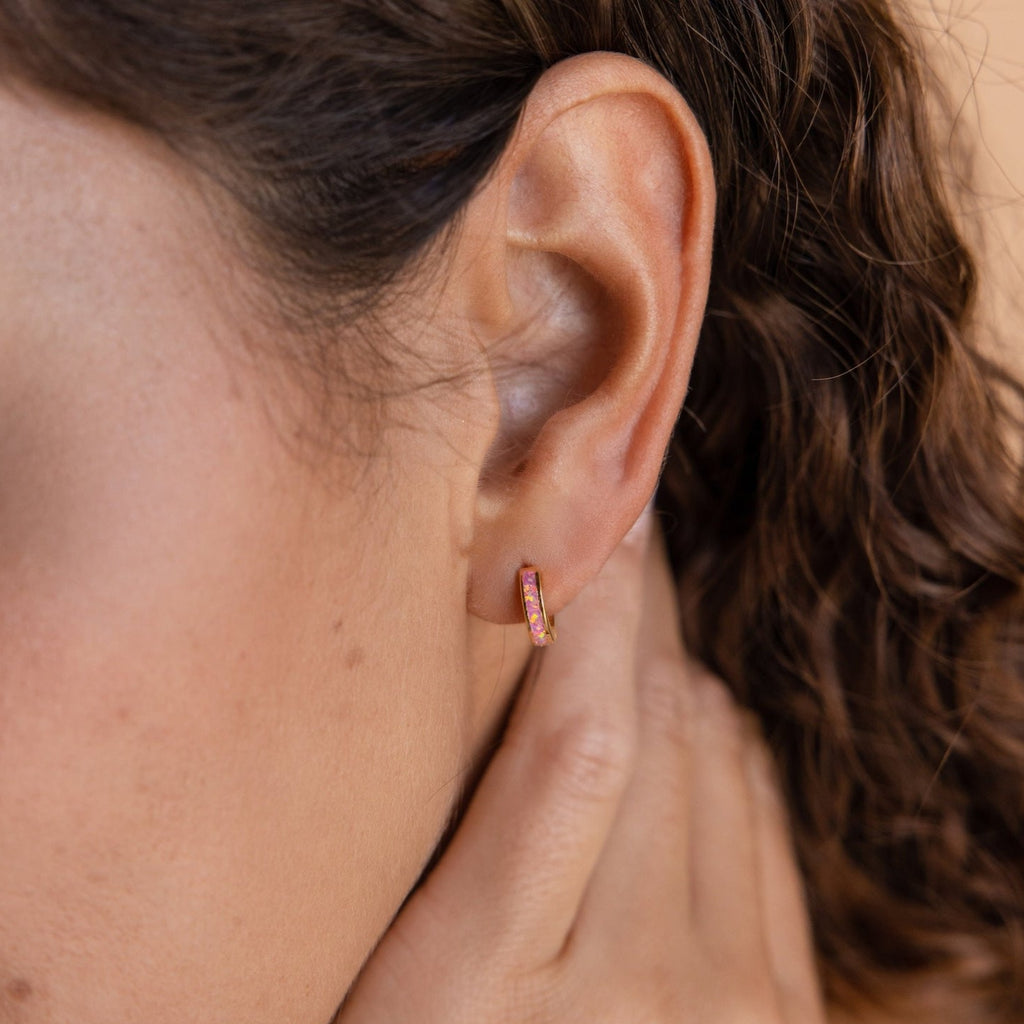 Close-up of a woman wearing Pink Opal Inlay Huggies, delicately showcased as she gently touches her neck.