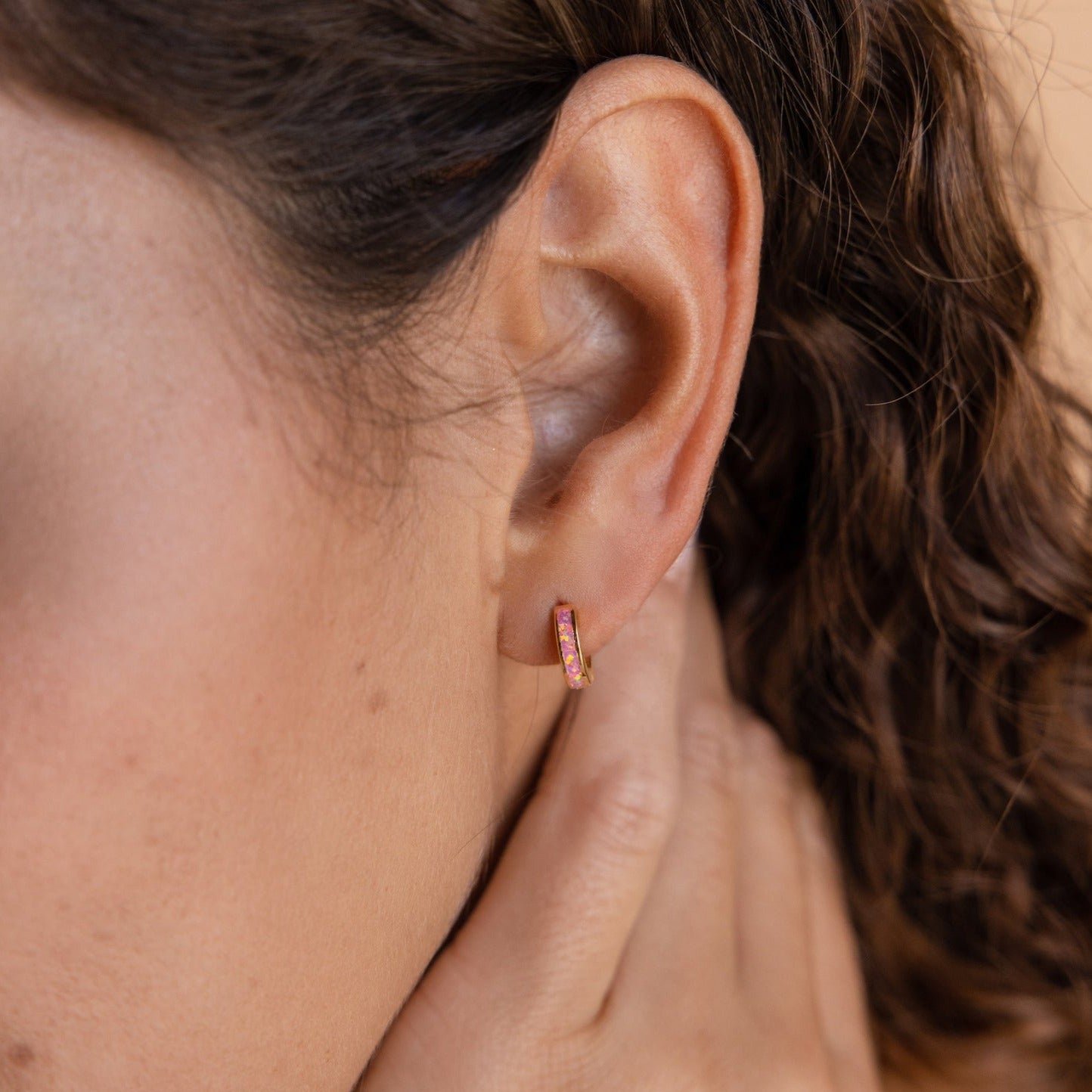 Close-up of a woman wearing Pink Opal Inlay Huggies, delicately showcased as she gently touches her neck.