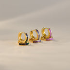 The Lavender Opal Inlay Huggies, a set of three minimalist hoop earrings with colorful iridescent accents, including a purple opal shimmer, are displayed on a soft beige background.