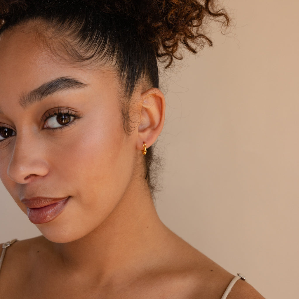 Woman with curly hair in a bun, wearing Link Huggies and a dainty chain earring in an elegant stack, looks at the camera against a beige background.
