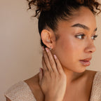 Woman with curly hair and neutral makeup touches her Link Huggies earrings, looking thoughtfully to the right.
