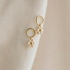 Flower Pearl Drop Earrings evoke vintage charm with their gold hoops and delicate pearl clusters, showcased against a soft, cream-colored fabric background.