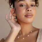 A woman wearing Flower Pearl Drop Earrings gently touches her earring and smiles softly.