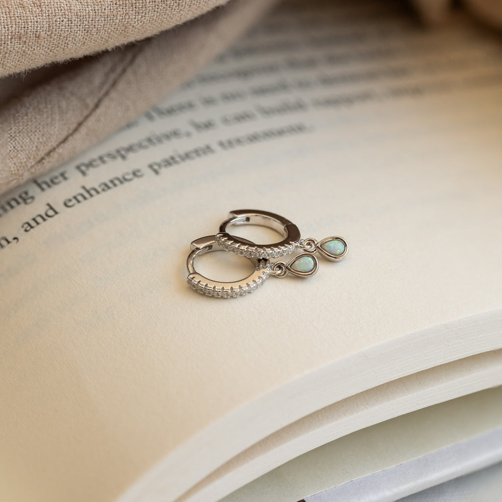 A pair of Opal Drop Huggies with turquoise stones rests on an open book.