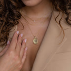A woman wearing a Custom Fingerprint Necklace in Rose Gold with an engraved pendant and a beige blazer touches her chest—an elegant, sentimental gift idea.