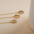Three gold Custom Fingerprint Necklaces with round pendants rest on a beige surface beside a white object. Each personalized necklace captures your unique touch, making it a meaningful keepsake.