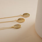 Three gold Custom Fingerprint Necklaces with round pendants rest on a beige surface beside a white object. Each personalized necklace captures your unique touch, making it a meaningful keepsake.