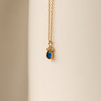 The Lorelei Sapphire Teardrop Necklace features a gold chain with a sapphire teardrop pendant and clear stones, creating an elegant, timeless accessory perfect for any outfit.