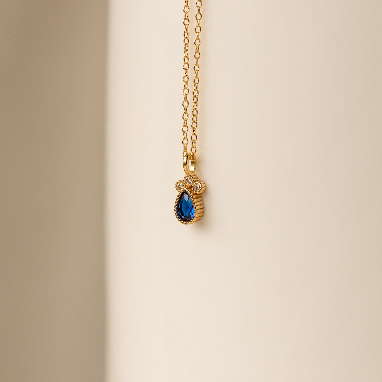 The Lorelei Sapphire Teardrop Necklace features a gold chain with a sapphire teardrop pendant and clear stones, creating an elegant, timeless accessory perfect for any outfit.