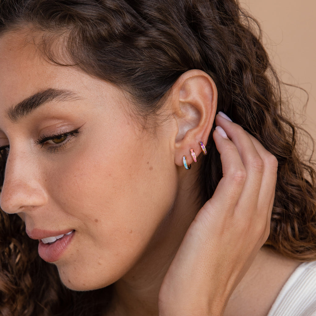 A woman with curly hair wearing Pastel Opal Inlay Huggies.