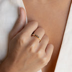 A hand wearing the Helena Black Diamond Ring, featuring gold accents, rests against a cream-colored fabric background for an edgy yet professional look.