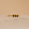 The Helena Black Diamond Ring is a delicate vintage gold ring with three black square stones and small clear gems on the band, set against a beige background for an edgy, professional look.