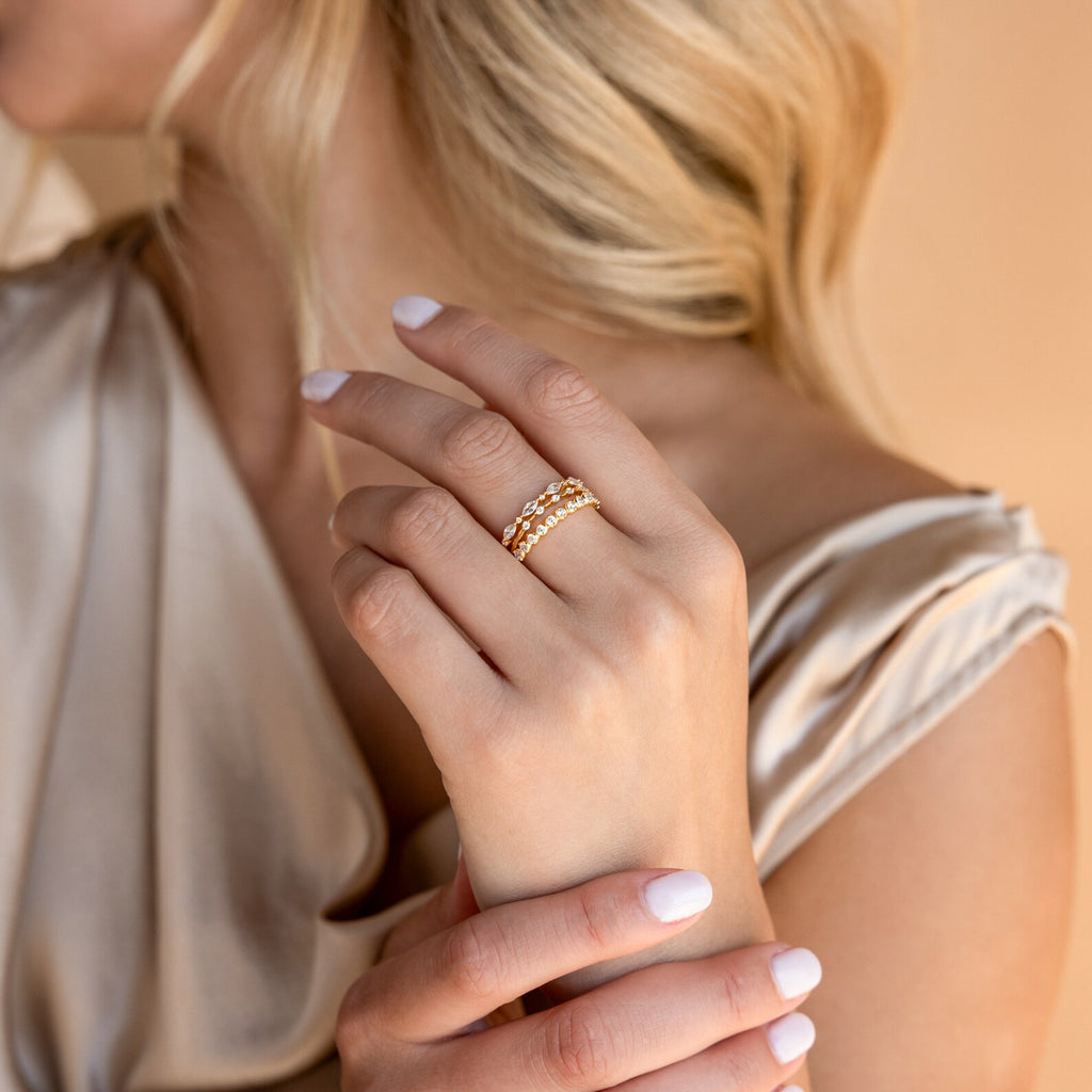 An elegant blonde woman touches her neck in a silky beige dress, wearing the Crystal Stacking Ring Set in Sterling Silver adorned with sparkling crystals.