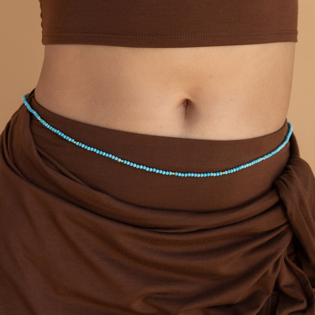A person wearing a brown crop top and brown sarong enhances their look with Beaded Belly Chains for a stylish boho-chic touch.
