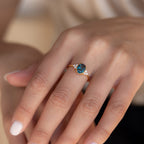 A hand wearing the Elizabeth Blue Topaz Ring in 18K Gold—a vintage boho ring with an oval blue gemstone and small clear stones on each side.